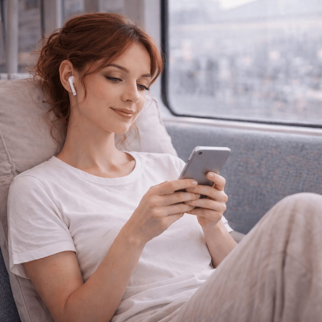 Femme souriante étudiant une formation en hypnose ericksonienne et EFT en ligne sur son téléphone dans les transports en commun
